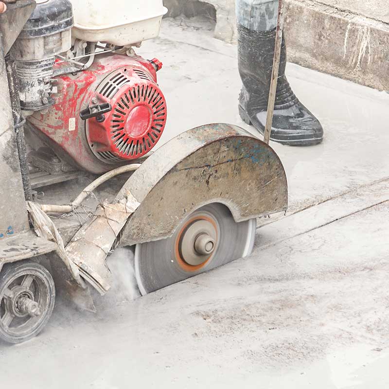 Arbeiter, der eine Diamantsägeblattmaschine verwendet, die eine Betonstraße auf der Baustelle schneidet